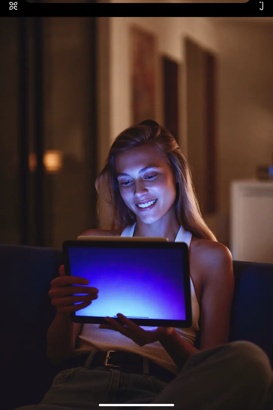 Woman relaxing at home on a video call at night, lit by her tablet screen